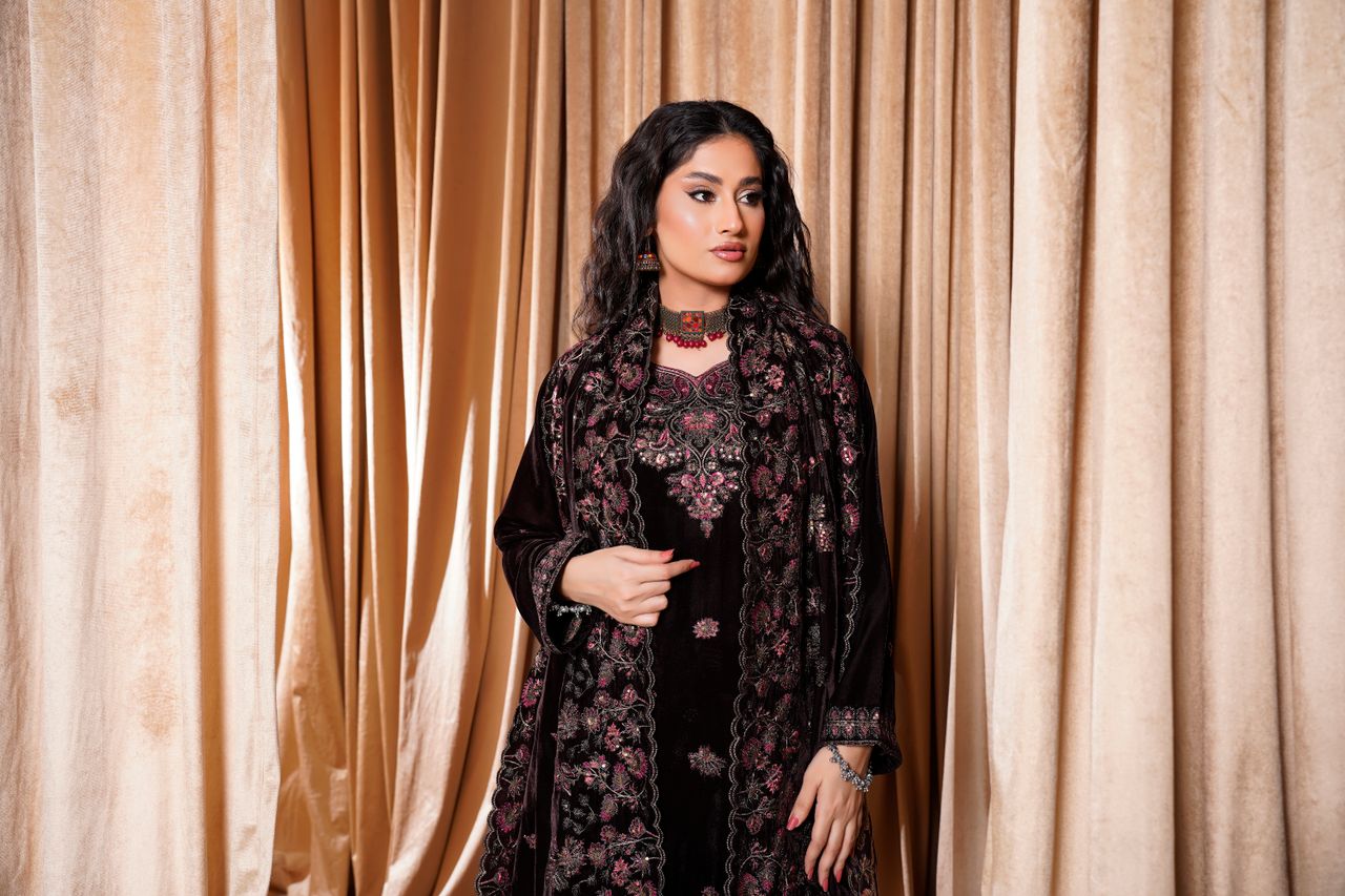 Stylish fashion model wearing a luxurious velvet embroidered dress against curtain backdrop.